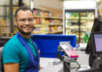 Operador de caixa sorridente em supermercado.