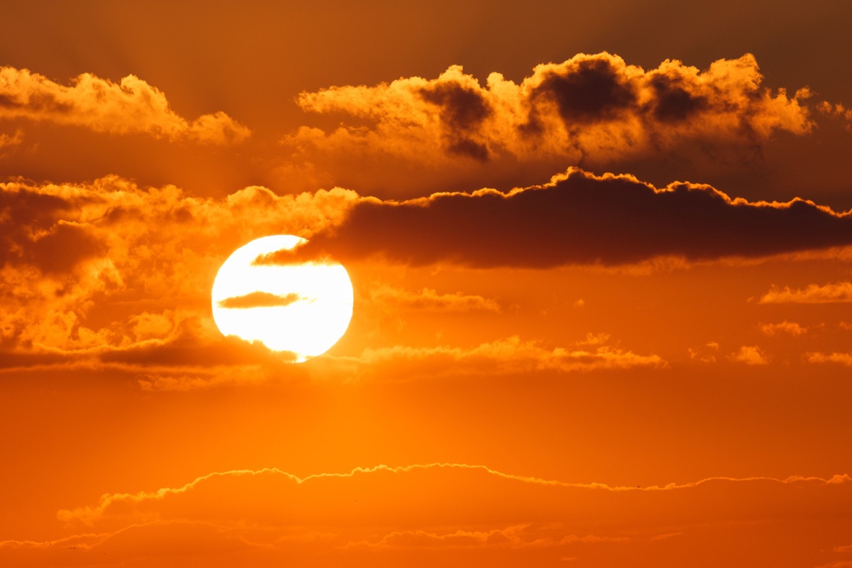 Imagem ilustrativa: sol alaranjado entre nuvens escuras no fim de tarde, cena que remete à dúvida sobre o plural de sol