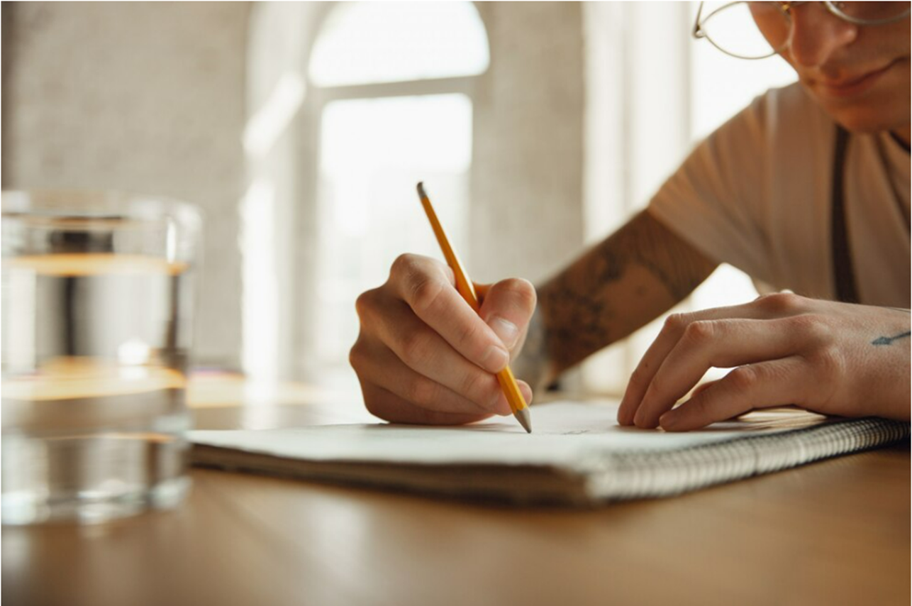 Ratificar e retificar. Pessoa escrevendo em um caderno, com foco na mão segurando um lápis, representando o processo de correção e revisão.