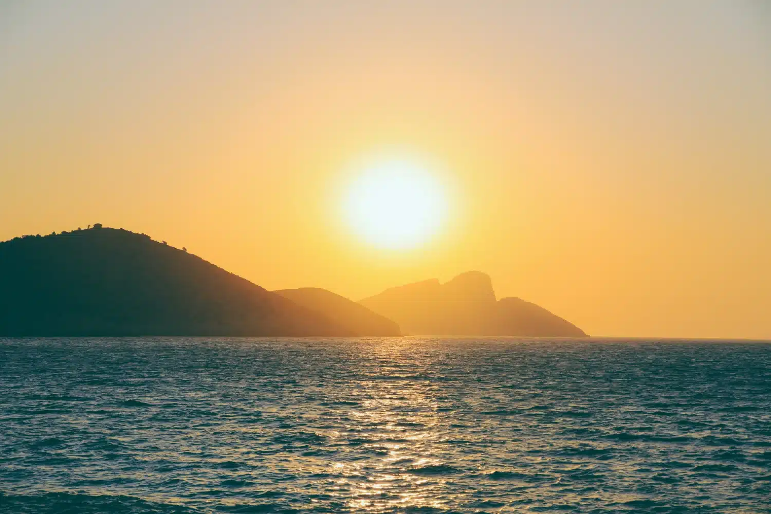Pôr do sol sobre o mar com montanhas ao fundo.