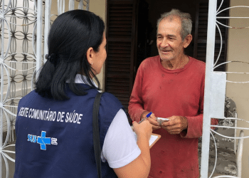 Agente comunitária do SUS realiza visita domiciliar e orienta morador.