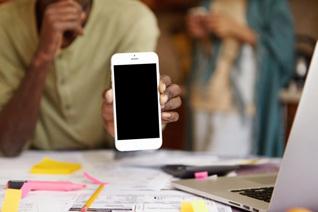People, technology and communication concept Close up shot of generic white mobile phone with copy space for your promotional content, held by African American male, who doing paperwork at home Uma das exceções do uso do celular na escola é para fins pedagógicos. Imagem: Freepik