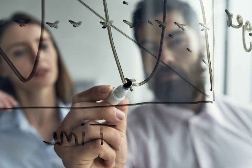 close up man explaining business analytics his female colleague with graph whiteboard A manipulação psicológica é o ato de influenciar outra pessoa de maneira enganosa para obter vantagem pessoal. Imagem: Freepik