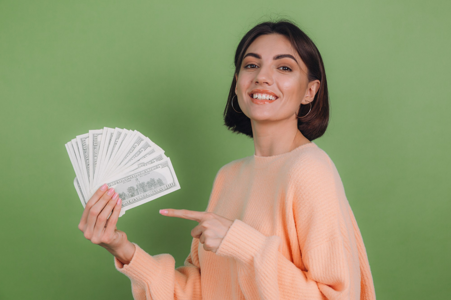 Veja o salário desta profissão que será um dos maiores destaques do mercado de trabalho. Mulher sorrindo com cédulas de dinheiro na mão em forma de leque, com a outra apontando para o dinheiro, a frente de um fundo verde.