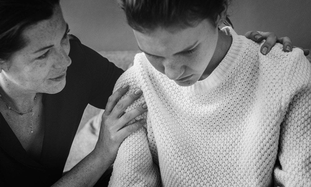 Mulher consolando jovem, possivelmente a filha, que encontra-se triste