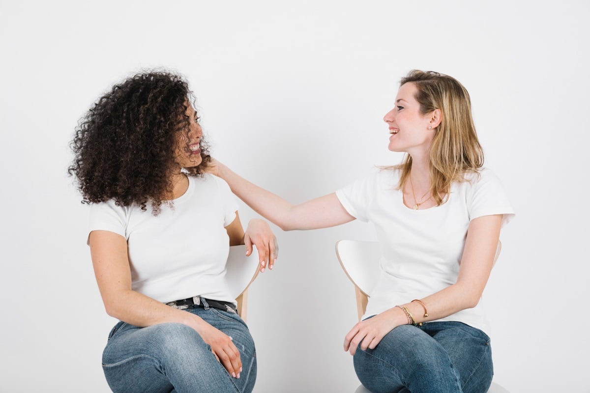 Duas mulheres sentadas rindo, com interação amigável, refletindo conexão