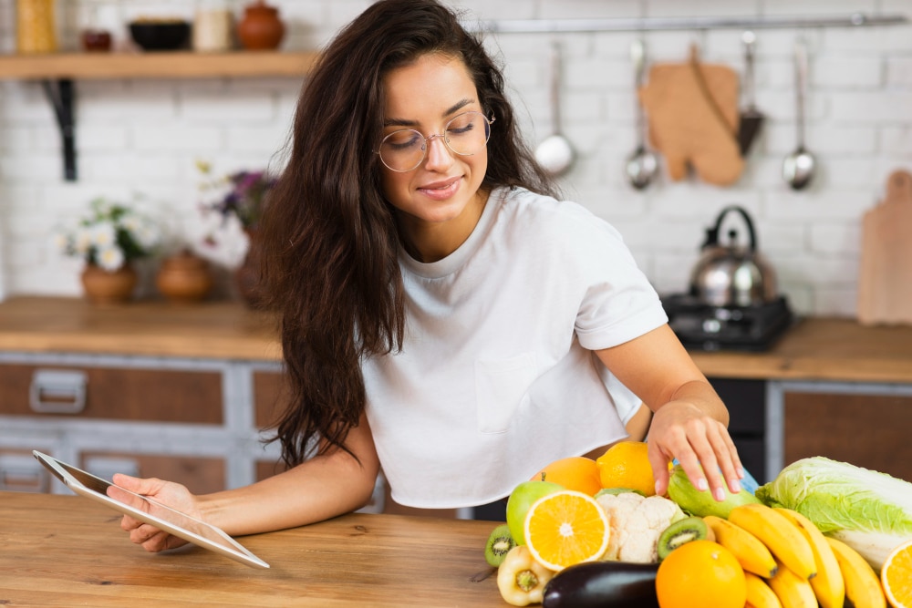 Mulher com camisa branca na cozinha pegando frutas para comer