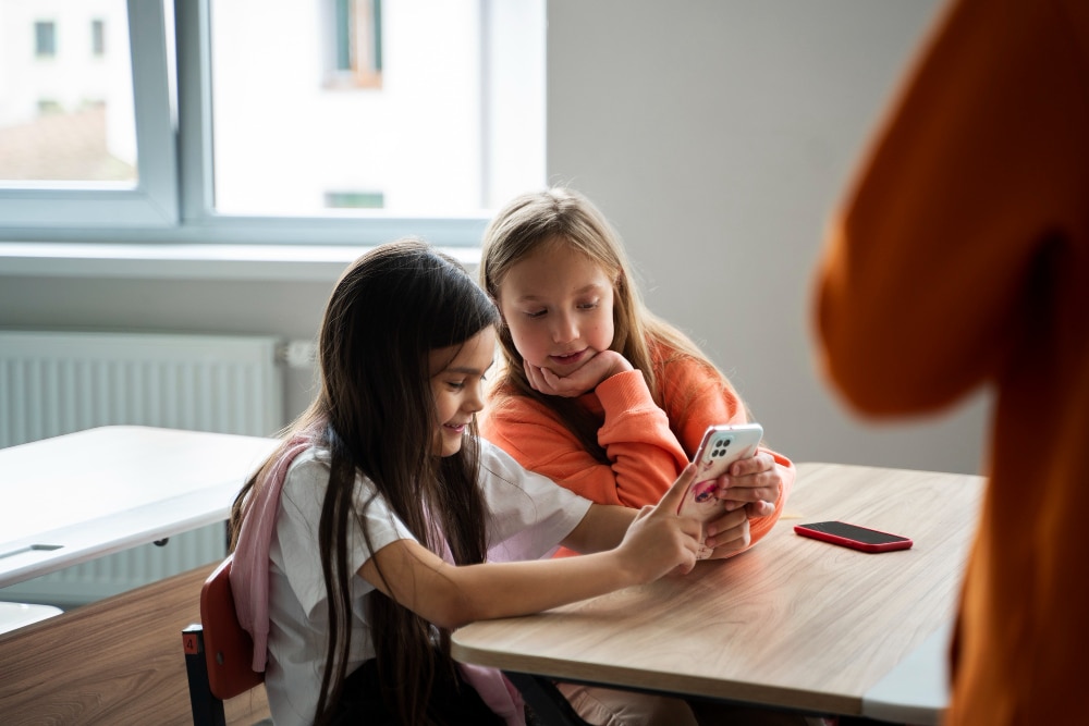 Duas meninas na sala de aula com o celular na mão