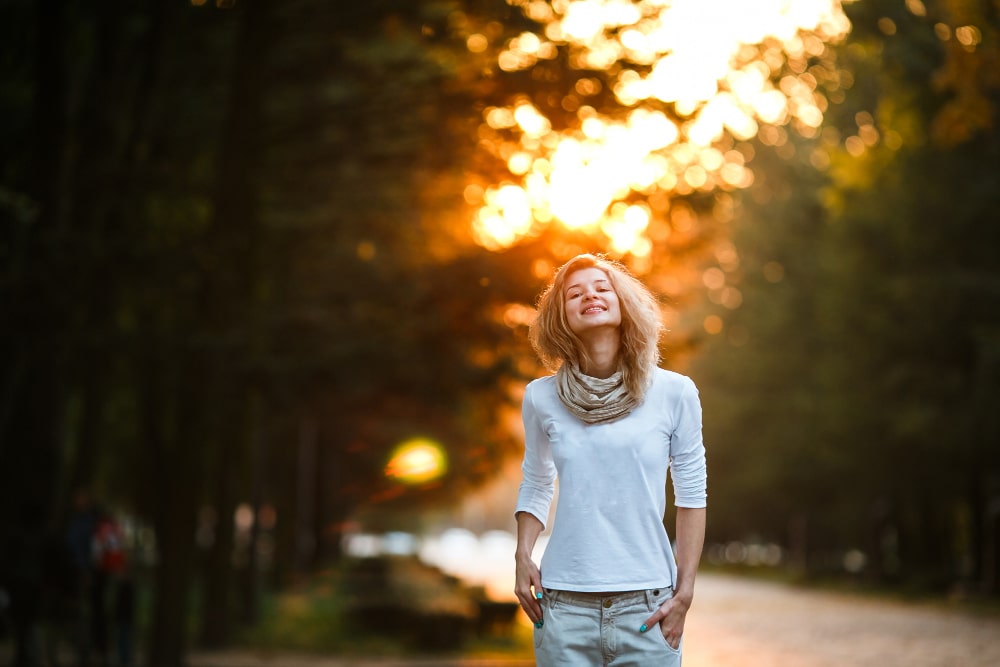 Mulher sorridente caminhando ao ar livre em um parque ao entardecer, expressando felicidade e bem-estar