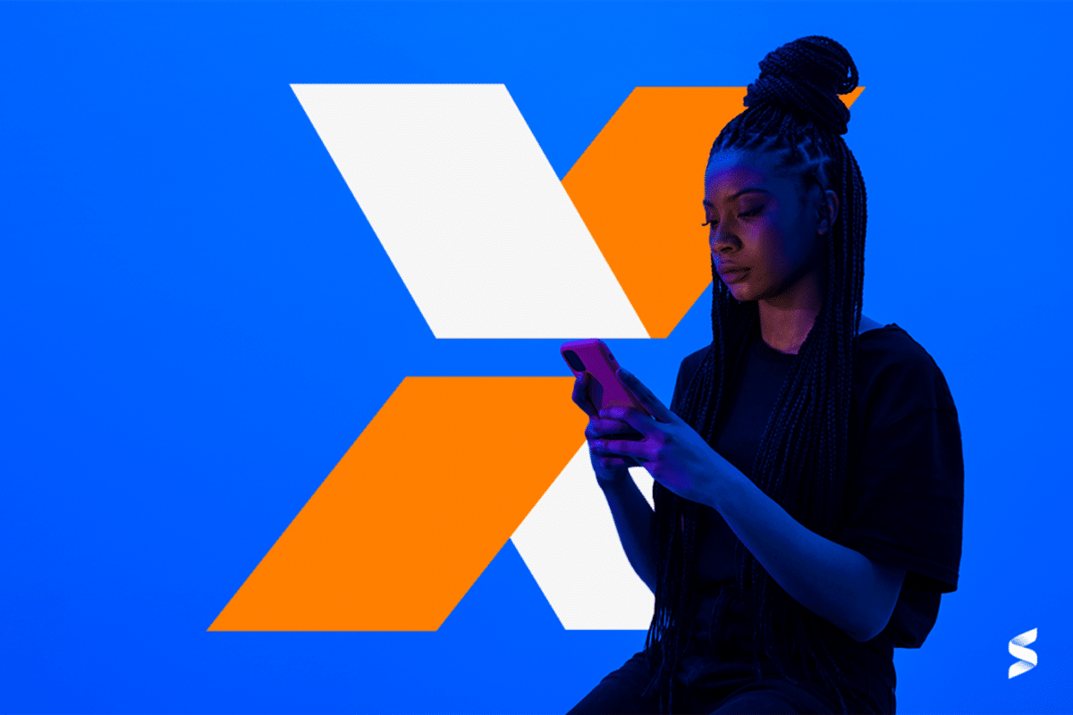 Símbolo da CAIXA ao fundo e jovem com celular nas mãos