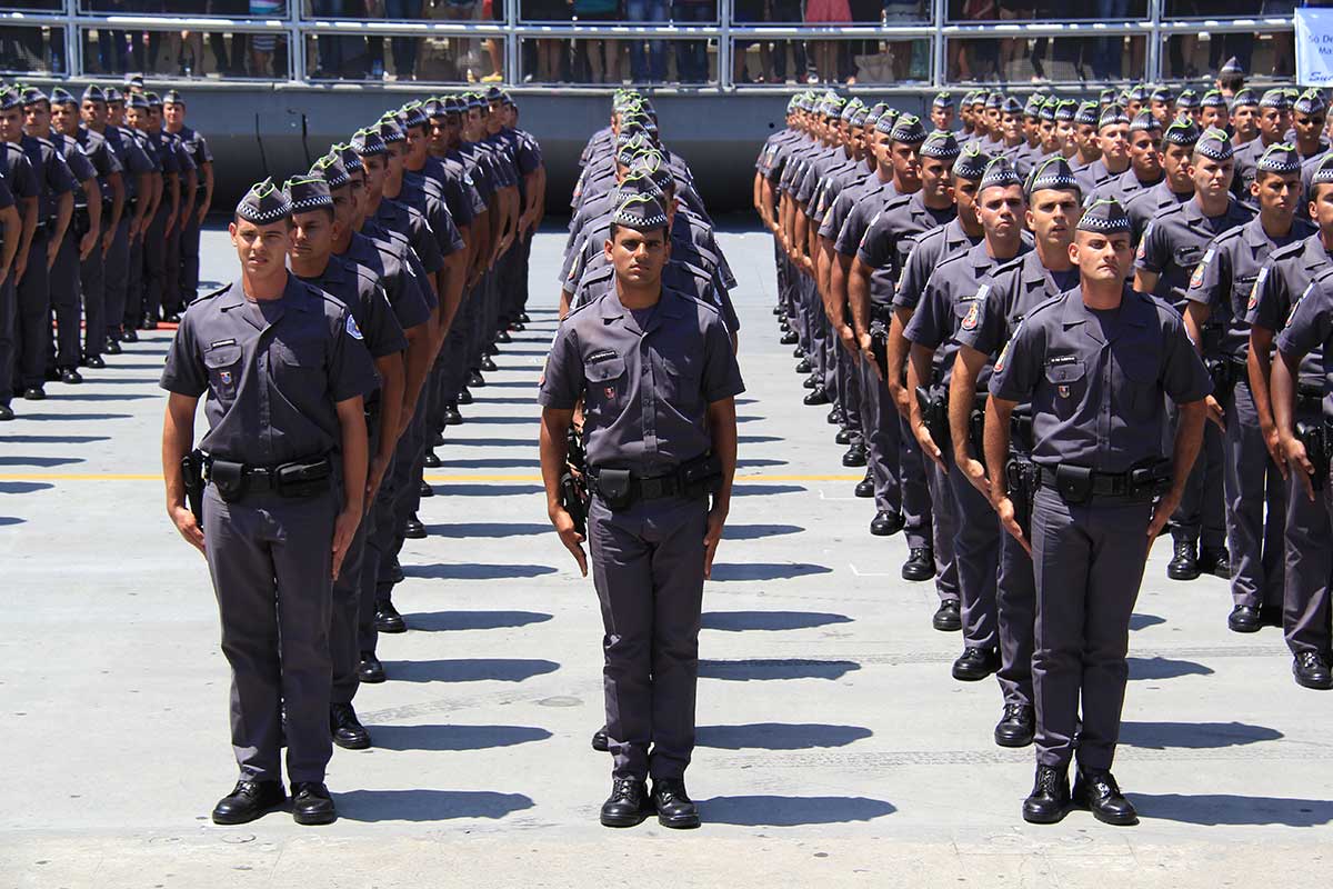 Formação de policiais militares fardados durante uma cerimônia oficial, alinhados em fileiras simétricas, demonstrando disciplina e organização