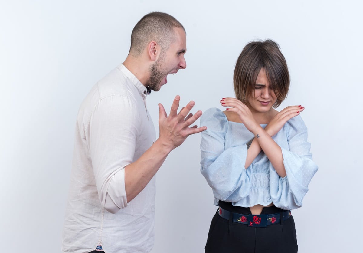 Homem gritando enquanto mulher se protege cruzando os braços, demonstrando desconforto em um conflito.