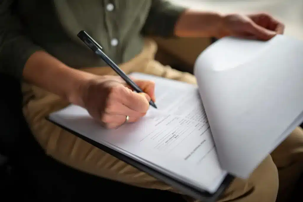 Organização de documentos para o processo seletivo da Prefeitura de Santa Cruz do Sul Pessoa preenchendo formulário em uma prancheta, revisando documentos para um processo seletivo