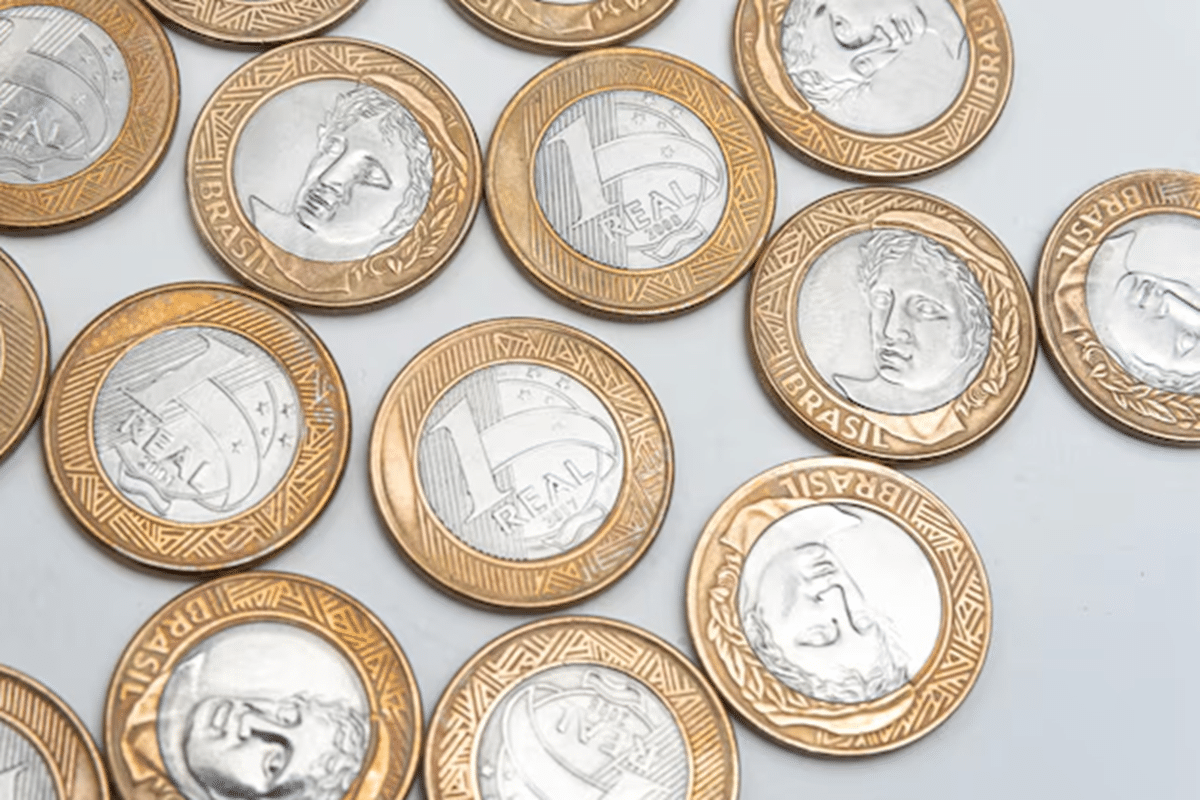 Moedas de 1 real do Brasil espalhadas sobre superfície branca