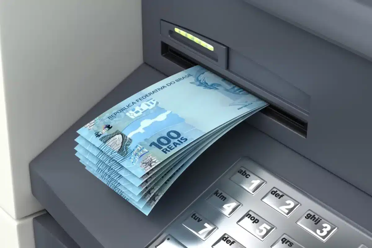Notas de 100 reais sendo sacadas de um caixa eletrônico
