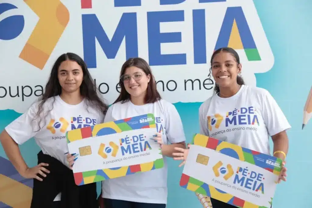 beneficiarias pe de meia comemoram incentivo financeiro Três estudantes segurando cartões do programa Pé-de-Meia e sorrindo.
