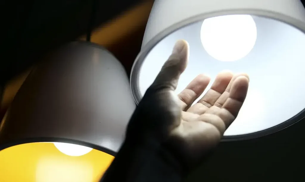 Quem tem direito ao desconto? Mão próxima a uma lâmpada acesa, simbolizando acesso à energia elétrica.