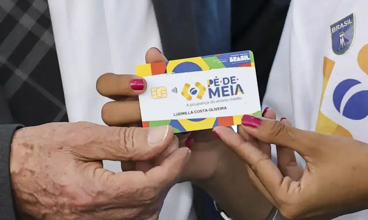 Cartão do Pé-de-Meia para estudantes do ensino médio Cartão do programa Pé-de-Meia sendo entregue a estudante, representando o incentivo financeiro para o ensino médio.