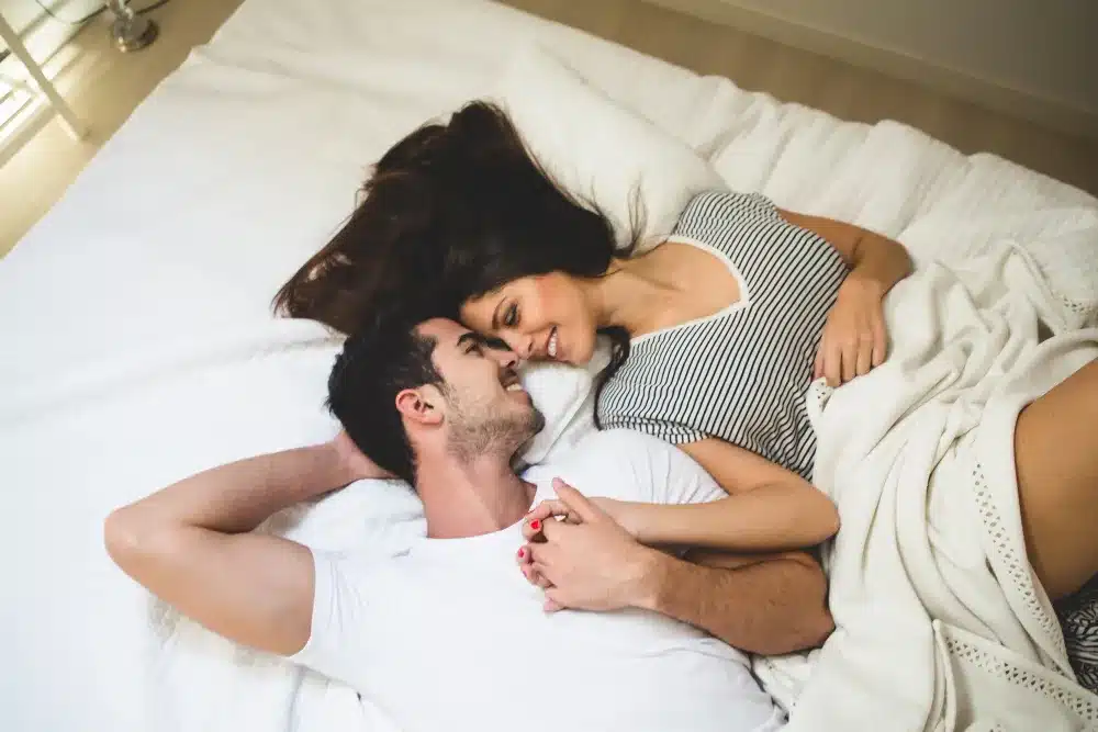 Casal apaixonado deitado na cama, sorrindo e segurando as mãos.