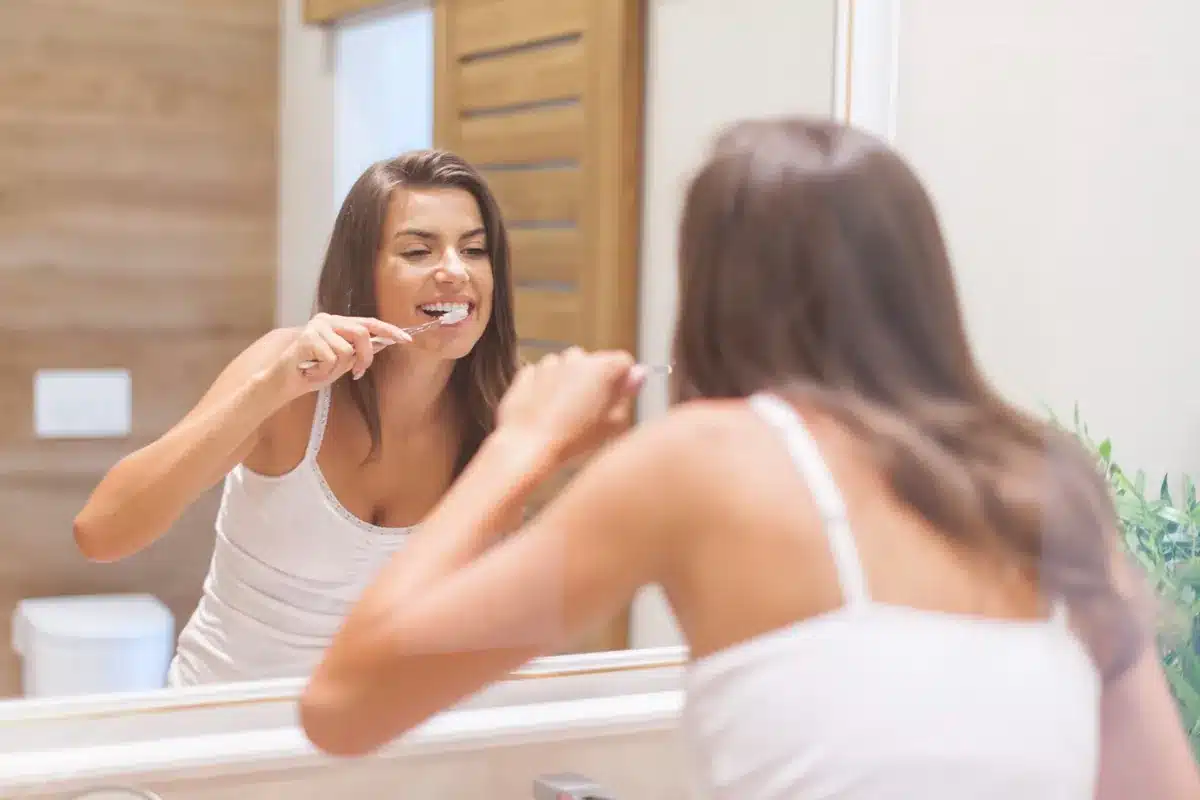 Mulher escovando os dentes em frente ao espelho do banheiro.