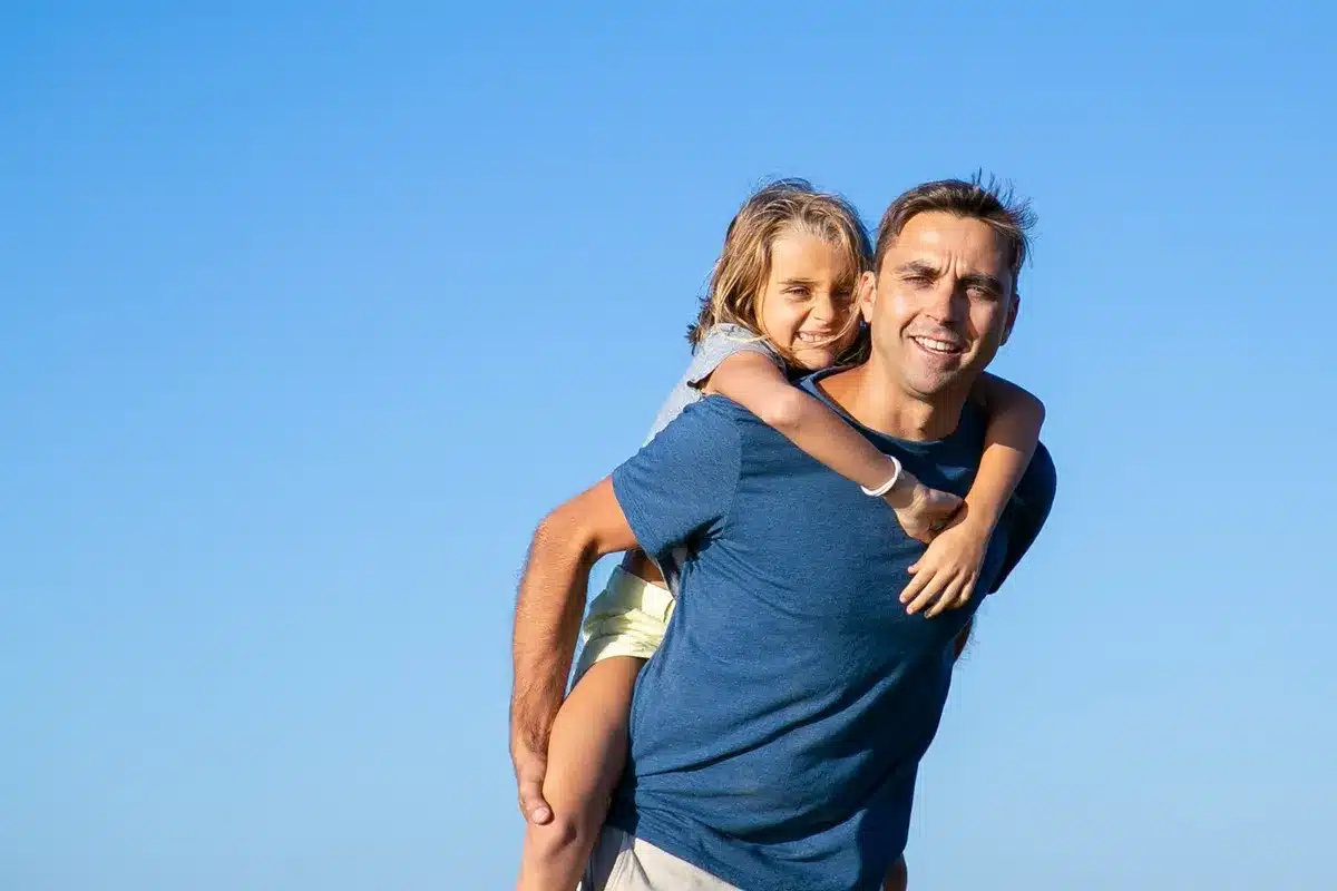 Pai carregando a filha nas costas, ambos sorrindo, representando conexão e afeto na relação familiar.