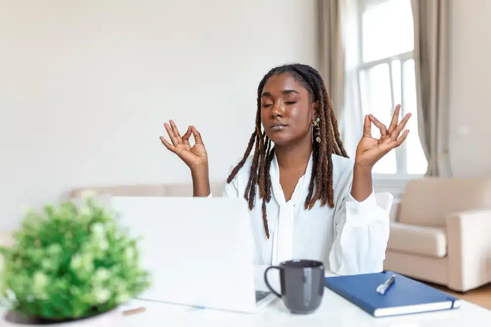 Desenvolvendo a Inteligência Emocional com Mindfulness e Meditação Pessoa praticando meditação enquanto trabalha no computador, simbolizando o uso de mindfulness para desenvolver inteligência emocional