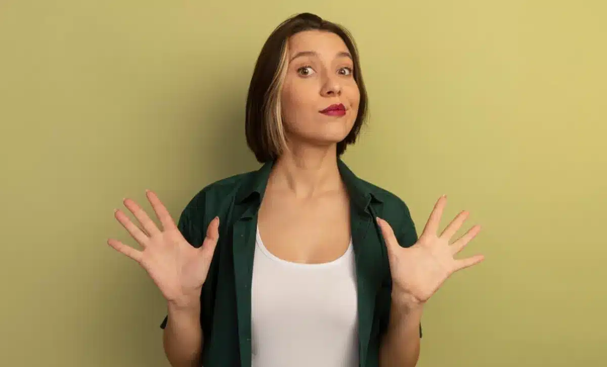 Mulher com expressão confusa, levantando as mãos como se estivesse dizendo 'não', em fundo verde.