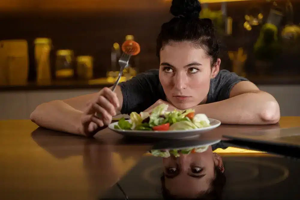Mulher olhando fixamente para um prato de salada com expressão séria.