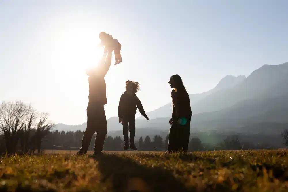 Família brincando ao ar livre ao pôr do sol, com pai levantando uma criança no ar.