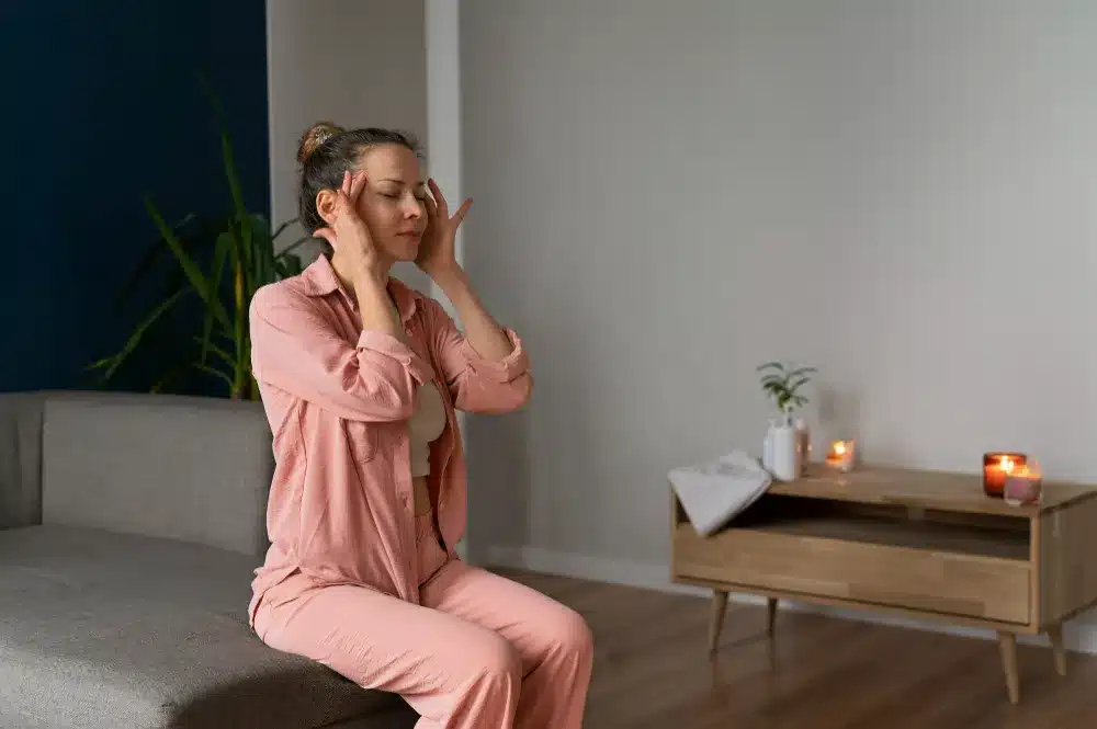 Gerenciando o estresse: pequenos hábitos para uma mente mais equilibrada Mulher sentada no sofá praticando técnicas de relaxamento para reduzir o estresse crônico.