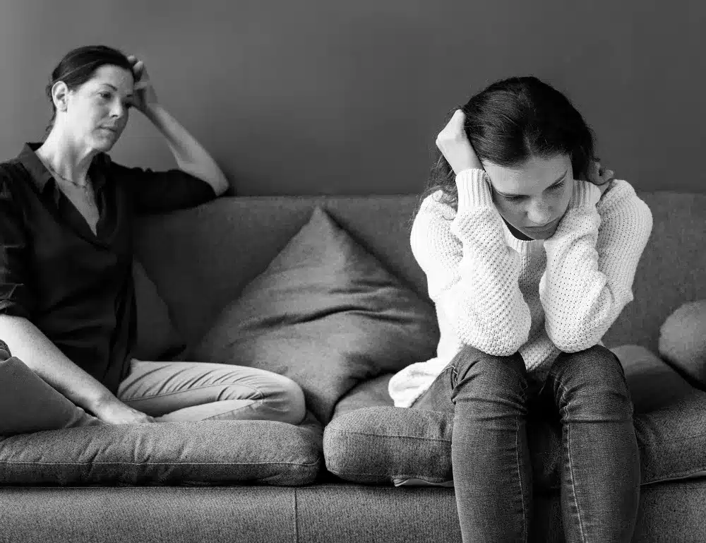 Mãe e filha sentadas no sofá, distantes emocionalmente, representando a falta de empatia na comunicação.