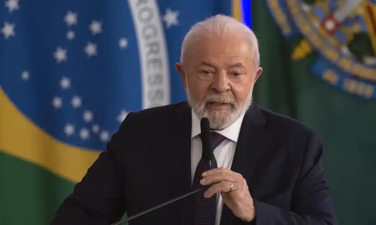 Presidente Lula discursa durante evento oficial, com bandeira do Brasil ao fundo