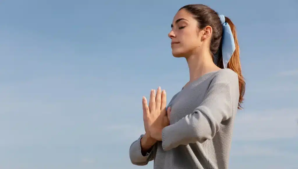 Meditação e positividade para uma vida mais feliz Mulher jovem meditando ao ar livre com as mãos em posição de prece, transmitindo paz e positividade