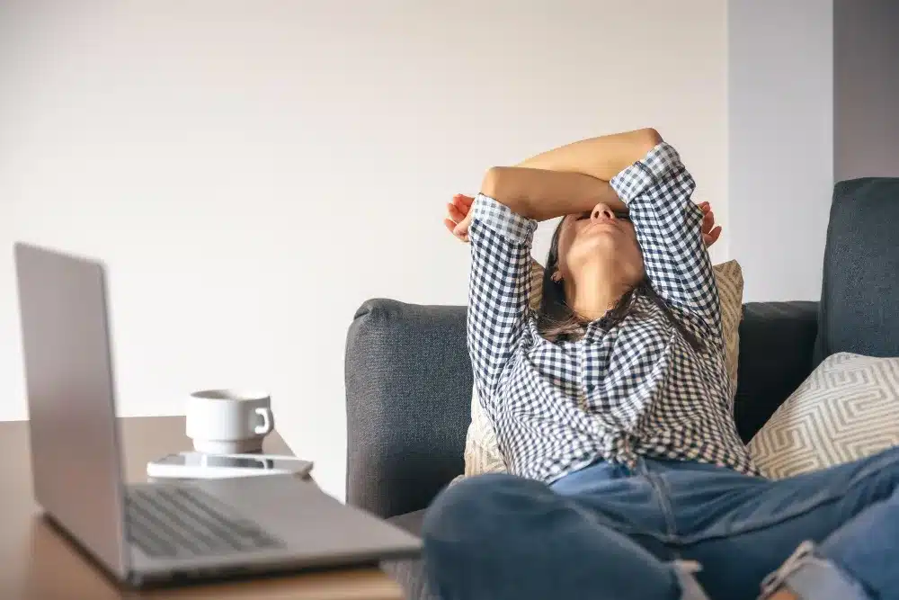 Mulher esgotada devido ao estresse do trabalho. Mulher exausta no sofá cobrindo o rosto com os braços, representando os efeitos do burnout.