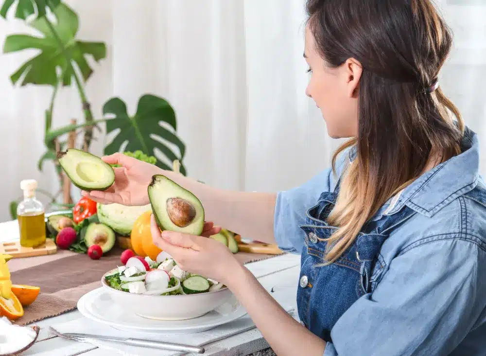 Preparo de Salada Nutritiva com Abacate Mulher preparando uma salada fresca com abacate, um alimento rico em gorduras saudáveis.