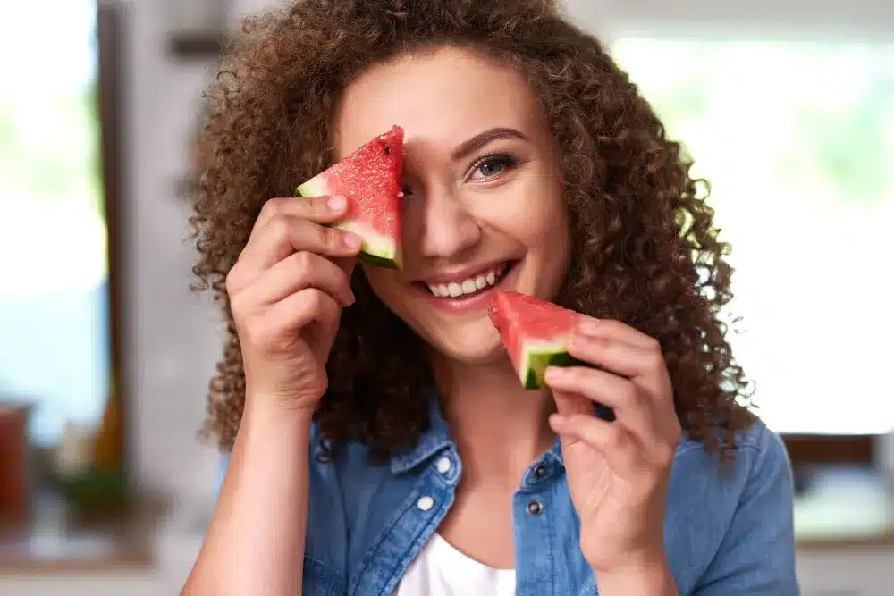 Benefícios da Melancia para Hidratação e Recuperação Muscular Mulher sorrindo e segurando pedaços de melancia, representando alimentação saudável e refrescante.