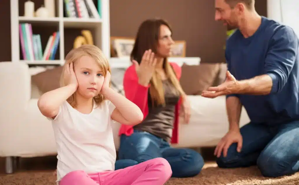 O impacto da negligência emocional nas crianças Criança tapando os ouvidos enquanto os pais discutem ao fundo, ilustrando os efeitos da negligência da saúde emocional.