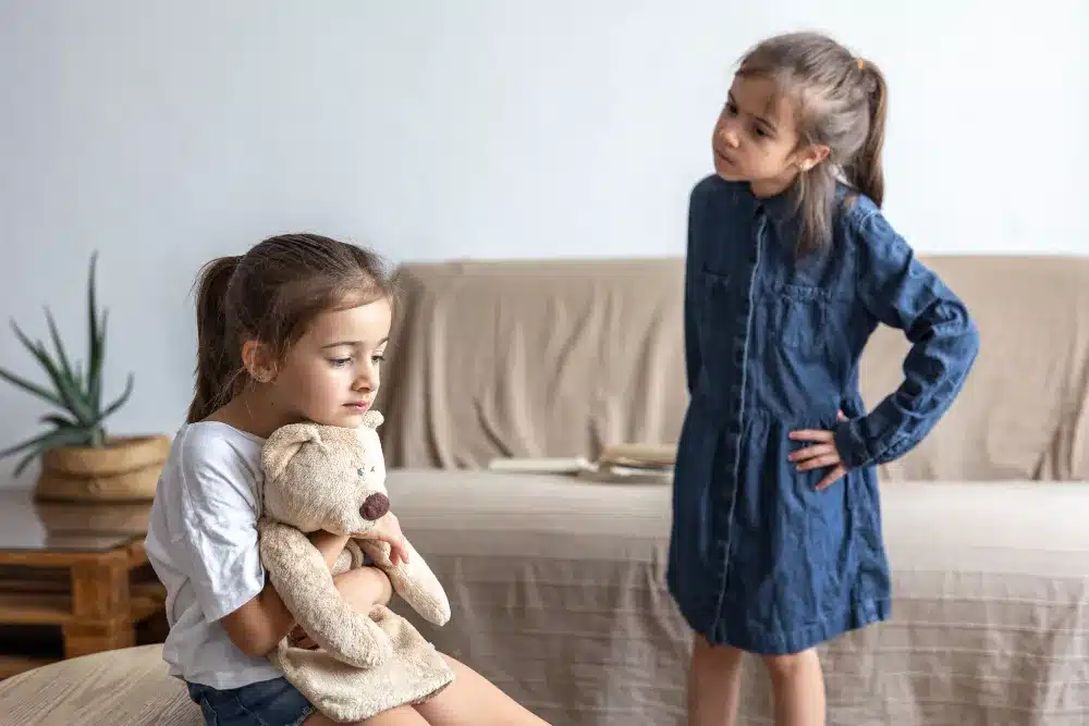 O Impacto da Privação Emocional na Formação de Vínculos Duas meninas, uma com um ursinho e a outra observando, simbolizando a privação emocional na infância.