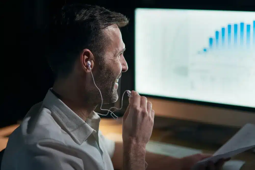 Profissional analisando gráficos financeiros em um computador, usando fones de ouvido.