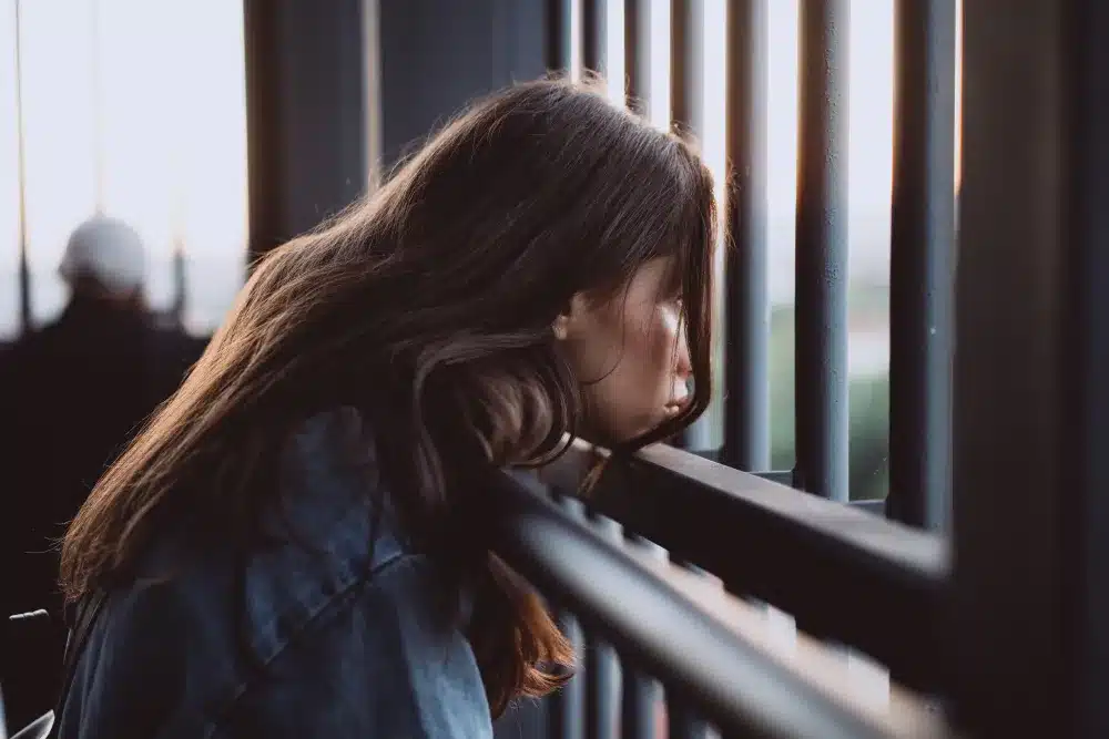 Jovem mulher de cabelos longos observando através das grades ao pôr do sol