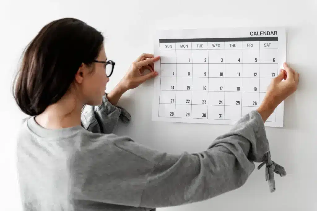 A importância da repetição na formação de hábitos Mulher fixando um calendário na parede, representando o papel da repetição na construção de hábitos