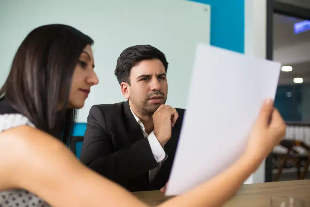 Resiliência diante de críticas: como lidar com feedbacks de forma construtiva Homem e mulher analisando documento, simbolizando a resiliência diante de críticas e feedbacks construtivos