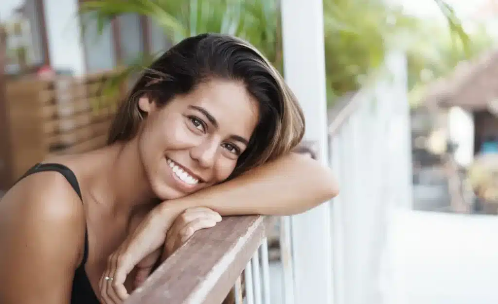 sorriso e personalidade Mulher sorrindo apoiada em uma grade, mostrando como o sorriso reflete a personalidade.