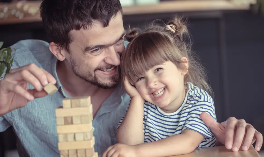 Pai e filha em momento de diversão: A verdade sobre herança genética" Pai e filha sorrindo juntos enquanto brincam de construir uma torre de blocos, ilustrando o vínculo familiar.