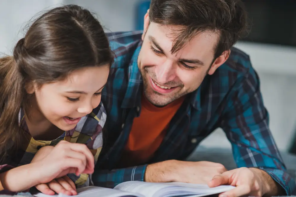 Pais e filhos aprendendo juntos Pai e filha sorrindo enquanto leem juntos, simbolizando a conexão e o aprendizado compartilhado.