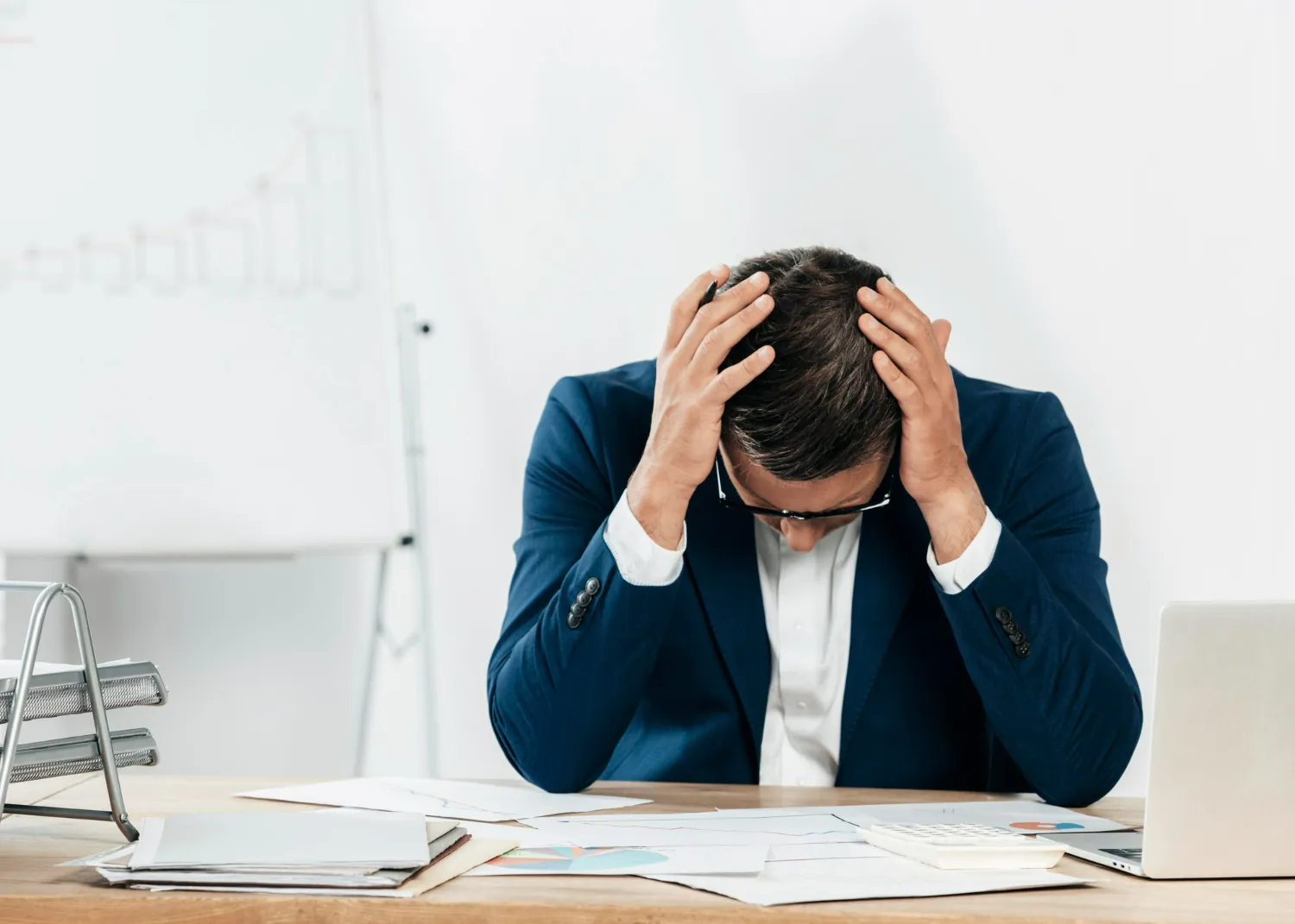 Homem em traje de negócios, com a mão na cabeça, expressando frustração e estresse em seu ambiente de trabalho.