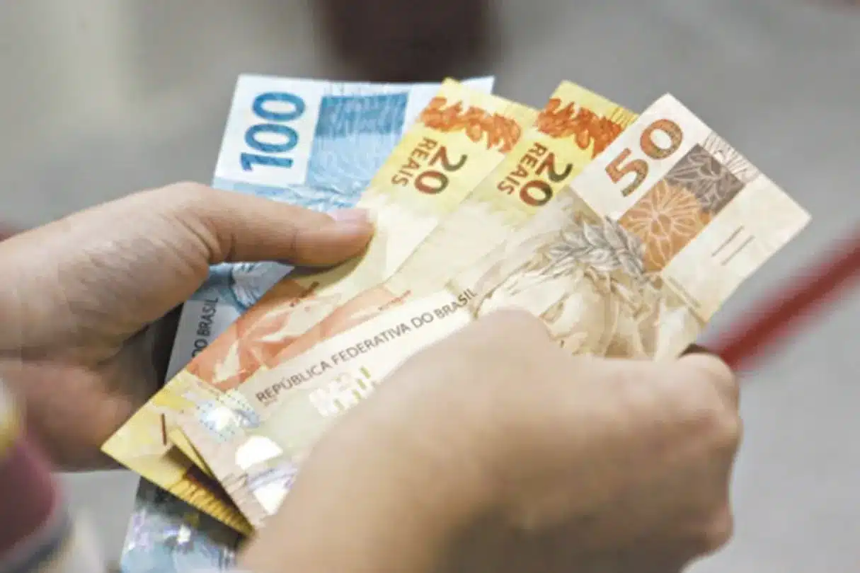 Notas de R$ 100, R$ 50 e R$ 20 sendo contadas, representando dinheiro em espécie.