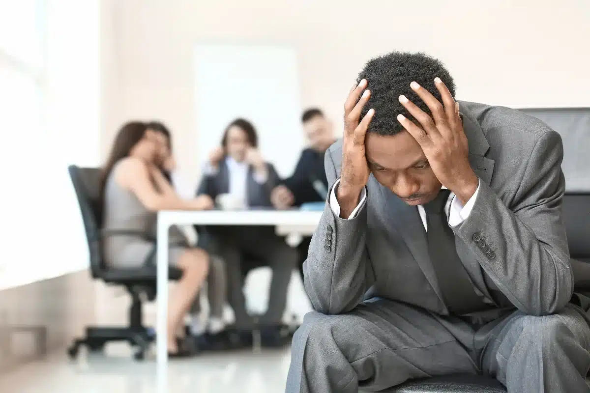 Solidão em ambiente de trabalho Homem sentado em uma cadeira com a cabeça baixa, demonstrando frustração durante uma reunião.