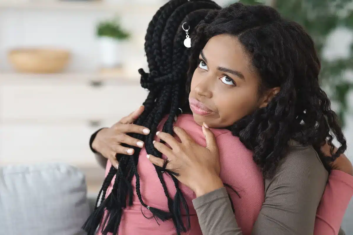 Mulher abraçando outra, mas com um olhar cético, expressando uma possível sensação de desconforto ou desconfiança.