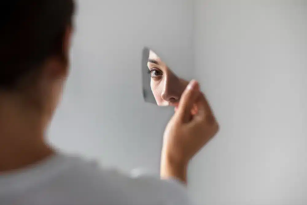 O reflexo da imperfeição e do autoconhecimento. Reflexo de uma mulher em um espelho quebrado, representando aceitação da imperfeição.